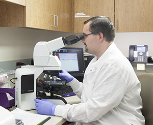 Un técnico de laboratorio sentado a una mesa, mirando por el microscopio.